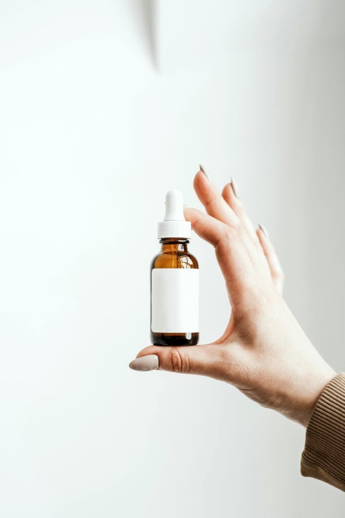 pexels-photo-8148744-8148744 A hand holding a minimalist dropper bottle on a white background, ideal for beauty product mockups.